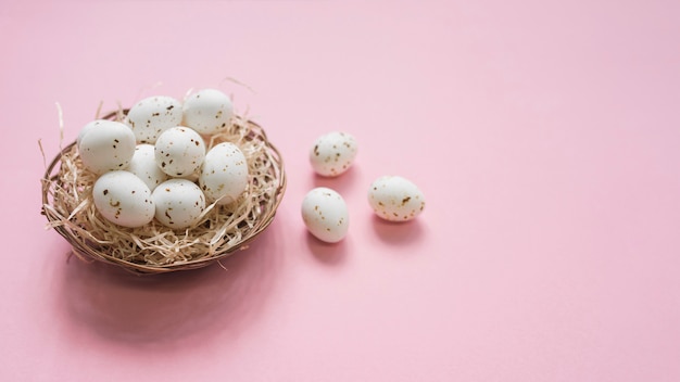 Foto gratuita huevos blancos en nido en mesa rosa