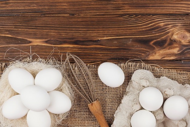 Foto gratuita huevos blancos en nido y en rejilla con batidor en mesa.