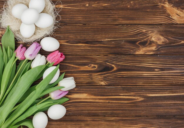 Huevos blancos en nido con tulipanes brillantes en mesa de madera