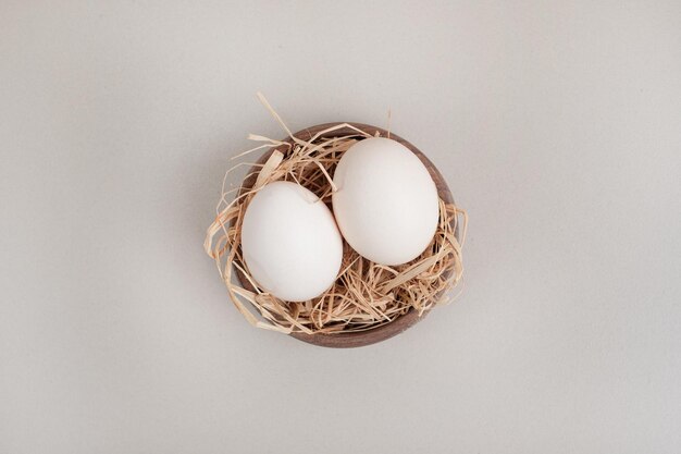 Foto gratuita huevos blancos de pollo frescos con heno en un tazón de madera.