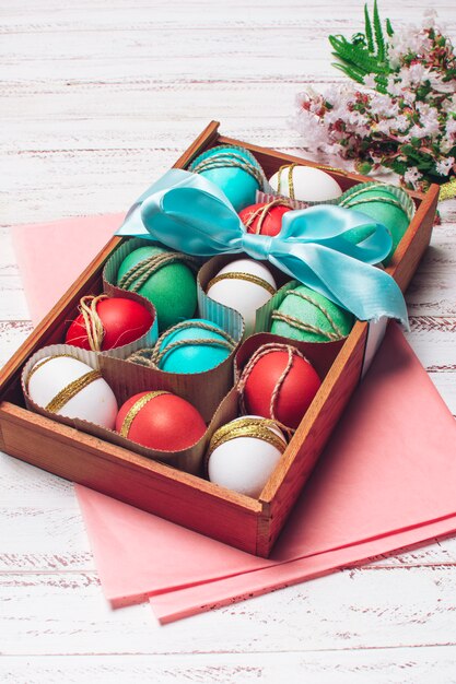 Huevos brillantes en caja en papel artesanal rosado cerca de ramo de flores