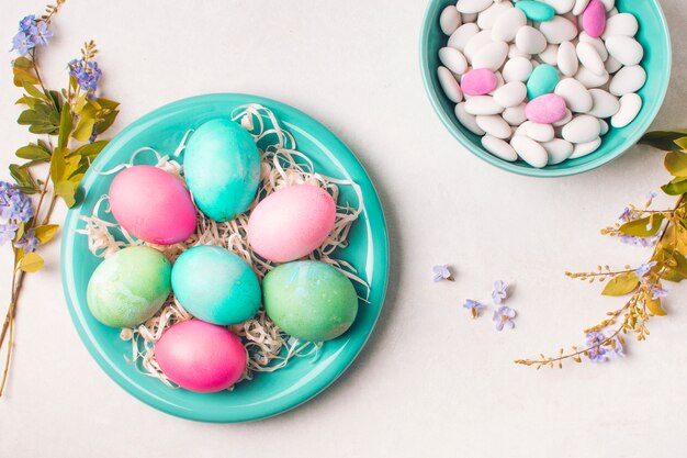 Huevos brillantes en un plato cerca de pequeñas piedras en un tazón y ramitas de flores