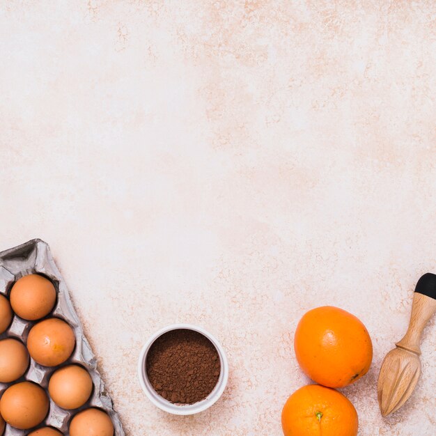 Huevos en caja; polvo de cacao; Cítricos y exprimidor de jugos de madera sobre fondo de concreto