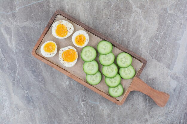 Huevos cocidos en rodajas con pepino sobre tabla de madera. Foto de alta calidad