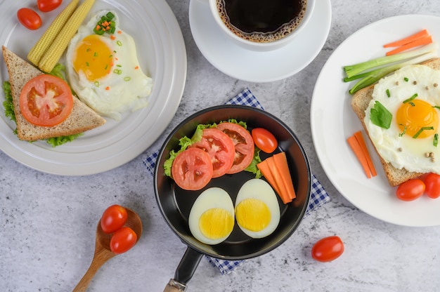 Huevos cocidos, zanahorias y tomates en una sartén con tomate en una cuchara de madera y una taza de café.