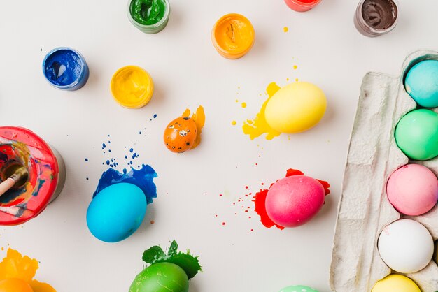 Huevos de colores brillantes cerca del recipiente, cepillo en lata y colores de agua