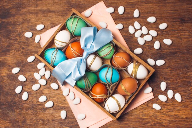 Huevos coloridos en caja en papel artesanal rosado cerca de pequeñas piedras