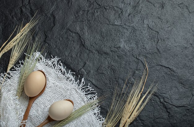 Huevos crudos y espigas de trigo en superficie oscura