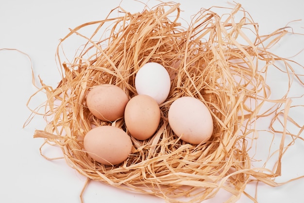 Huevos crudos en nido de pájaro sobre superficie blanca.
