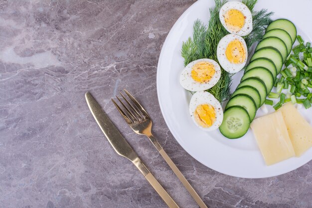 Huevos duros con hierbas picadas y pepinos en una placa blanca.