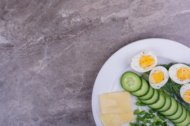 Huevos duros con pepinos en rodajas y hierbas en un plato blanco.