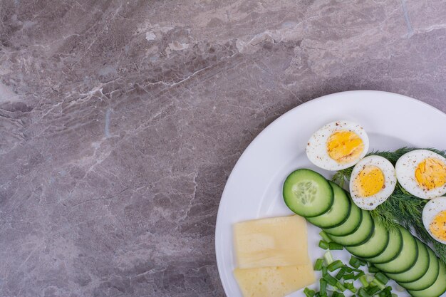 Huevos duros con pepinos en rodajas y hierbas en un plato blanco.