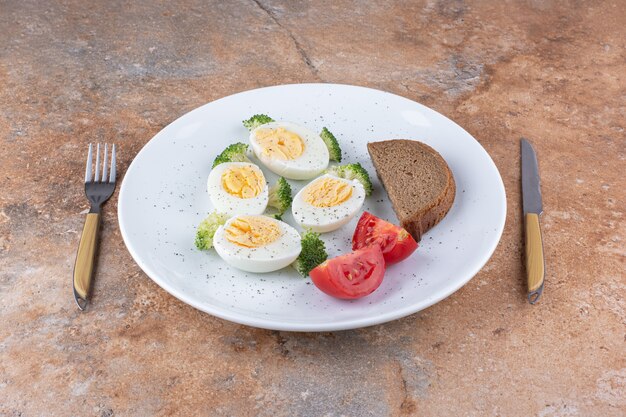 Huevos duros en un plato blanco con pan y verduras