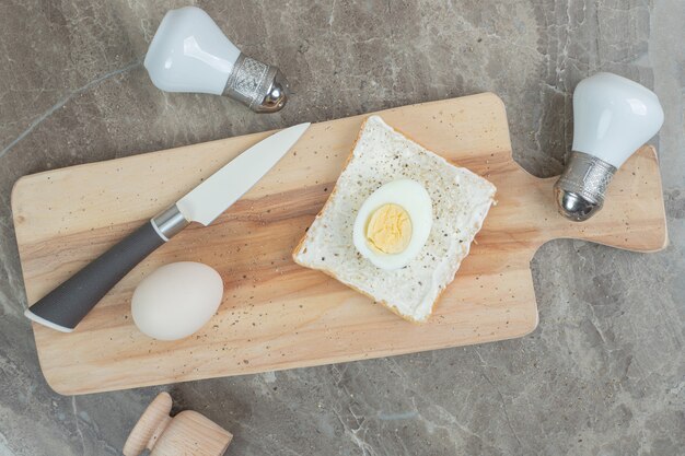 Huevos duros y rebanada de pan tostado sobre tabla de cortar con cuchillo y especias. Foto de alta calidad