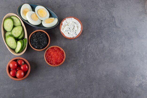 Huevos duros con salchichas y pepinos en rodajas colocados sobre fondo de piedra.