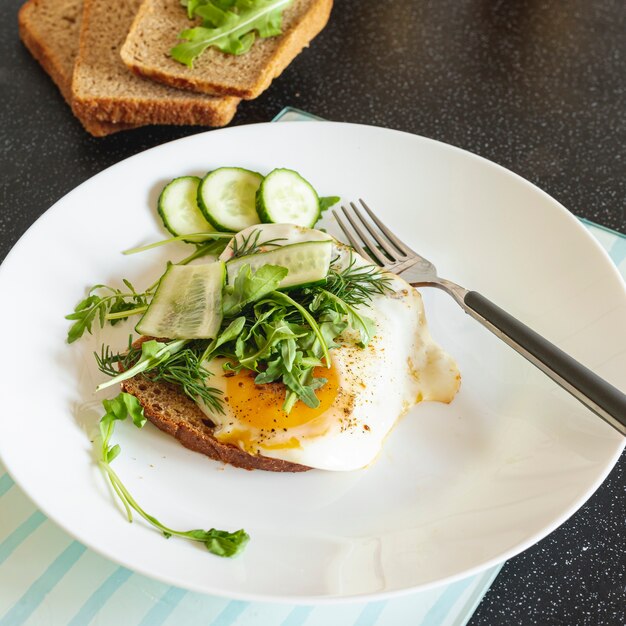 Huevos fritos con pepino y pan sobre una mesa negra