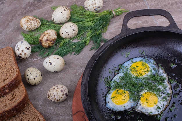 Huevos fritos en una sartén metálica con hierbas.