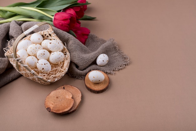 Huevos de gallina blanca en canasta con tulipanes rojos