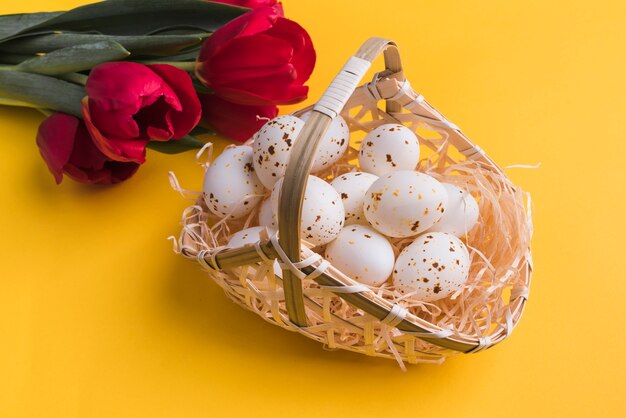 Huevos de gallina blanca en canasta con tulipanes