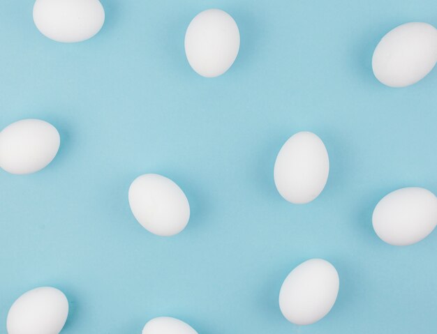 Huevos de gallina blanca esparcidos sobre mesa azul