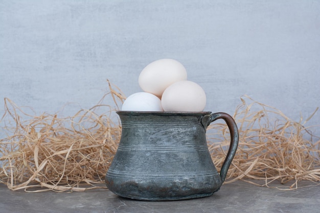 Huevos de gallina blanca fresca en taza antigua en heno. foto de alta calidad