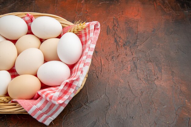 Huevos de gallina blanca vista frontal dentro de la canasta con toalla sobre la superficie oscura