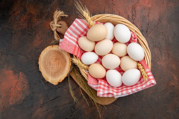 Huevos de gallina blanca vista superior dentro de la canasta con toalla sobre la mesa oscura