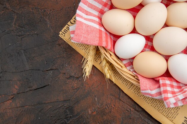 Huevos de gallina blanca vista superior dentro de la canasta con toalla sobre la mesa oscura