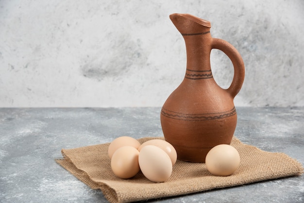 Huevos de gallina cruda fresca y botella antigua sobre superficie de mármol.