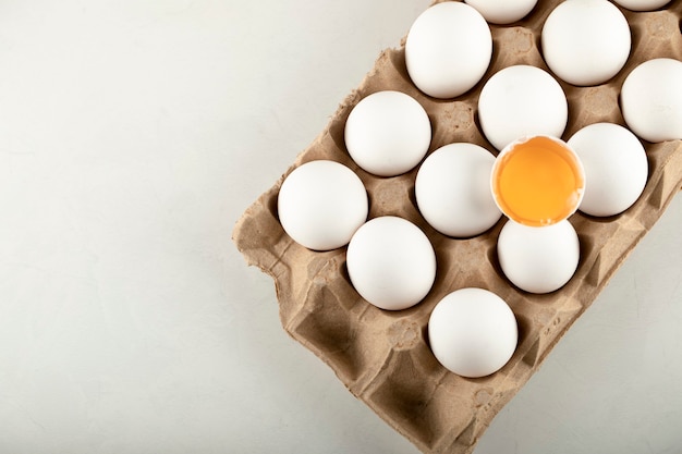 Huevos de gallina crudos en caja de huevos sobre una superficie blanca.