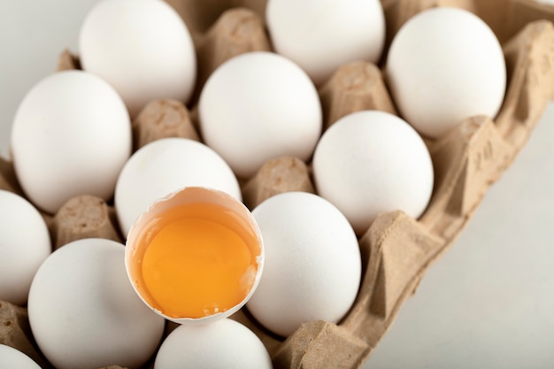 Huevos de gallina crudos en caja de huevos sobre una superficie blanca.