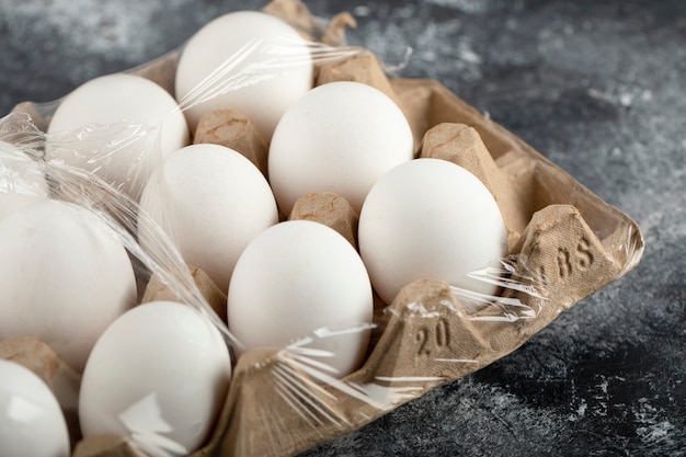 Huevos de gallina crudos en caja de huevos sobre una superficie de mármol.