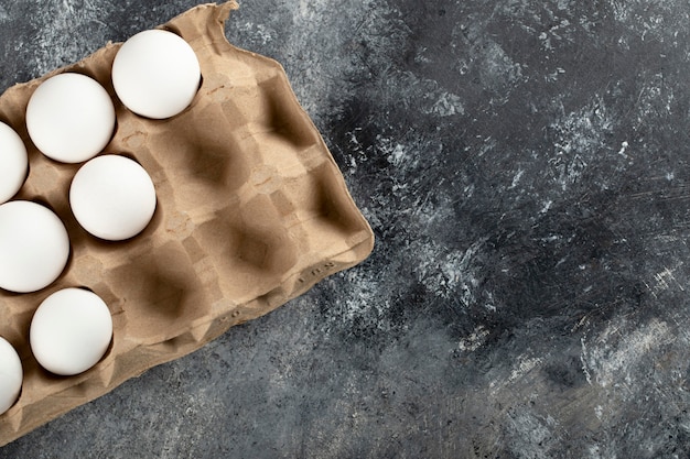 Huevos de gallina crudos en caja de huevos sobre una superficie de mármol.