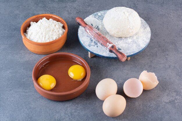 Huevos de gallina crudos frescos con harina colocados sobre la mesa de piedra.