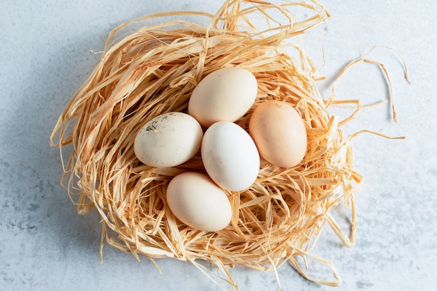 Huevos de gallina frescos en paja sobre superficie gris.