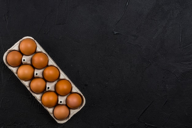 Foto gratuita huevos de gallina marrón en rejilla en mesa negro