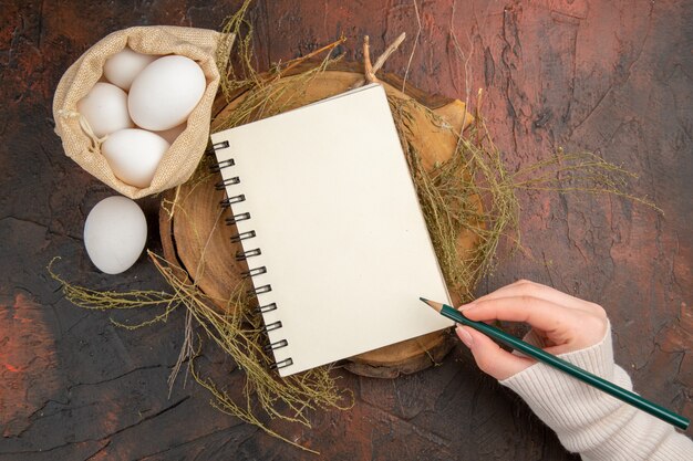 Huevos de gallina de vista superior dentro de la pequeña bolsa, escritura a mano en el cuaderno vacío