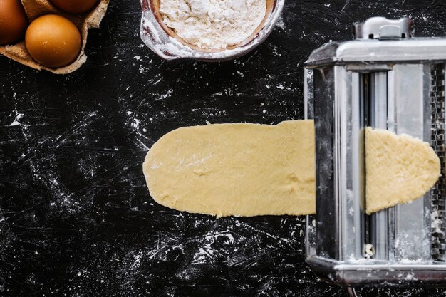 Huevos y harina cerca de la máquina de pasta con masa