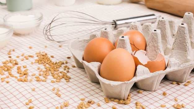 Huevos marrones en el cartón cerca del grano de trigo y batir sobre el mantel