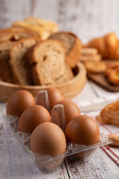 Huevos en paneles de plástico y pan que se coloca sobre una placa de madera blanca.