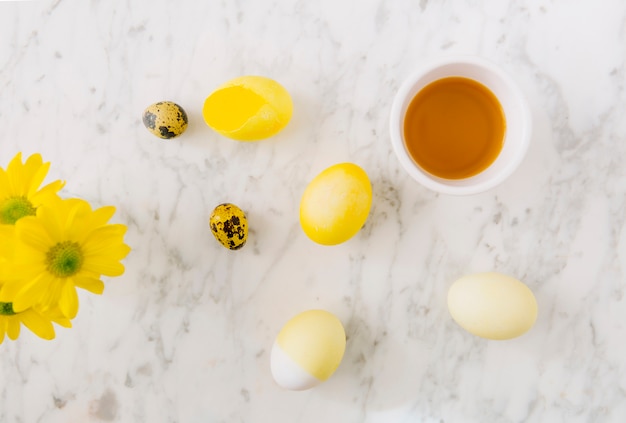 Huevos de Pascua amarillos cerca de flores frescas y tinte líquido