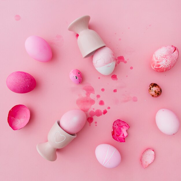 Huevos de Pascua blancos y rosados cerca de hueveras entre salpicaduras de tinte líquido