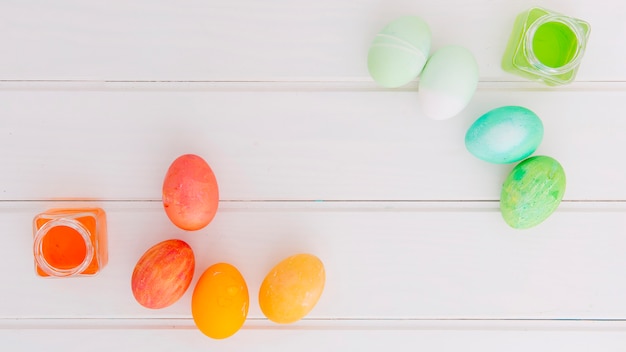 Foto gratuita huevos de pascua brillantes cerca de latas de líquido tinte en el escritorio