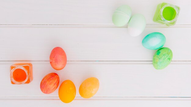 Huevos de Pascua brillantes cerca de latas de líquido tinte en el escritorio