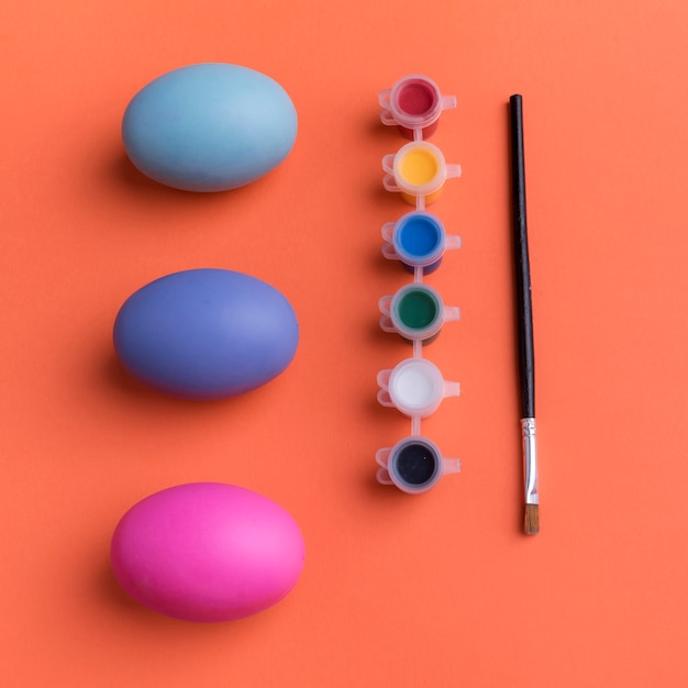 Foto gratuita huevos de pascua brillantes con pinturas en la mesa