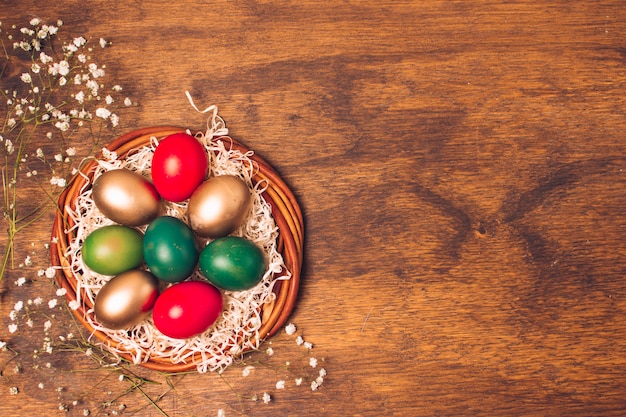 Huevos de Pascua brillantes en placa con oropel cerca de las plantas