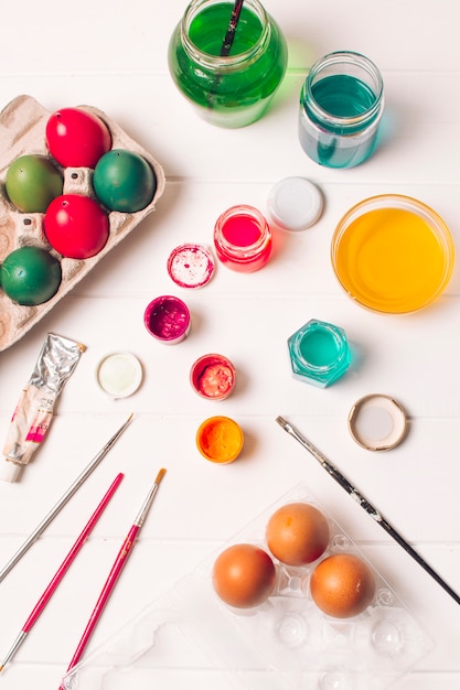 Foto gratuita huevos de pascua brillantes en recipientes cerca de pinceles y tinte líquido en latas