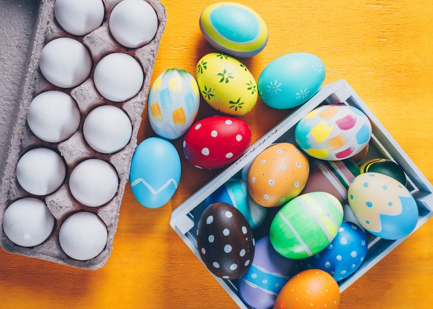 Huevos de Pascua en caja de madera y vista superior de cartón de huevos sobre fondo de madera amarillo