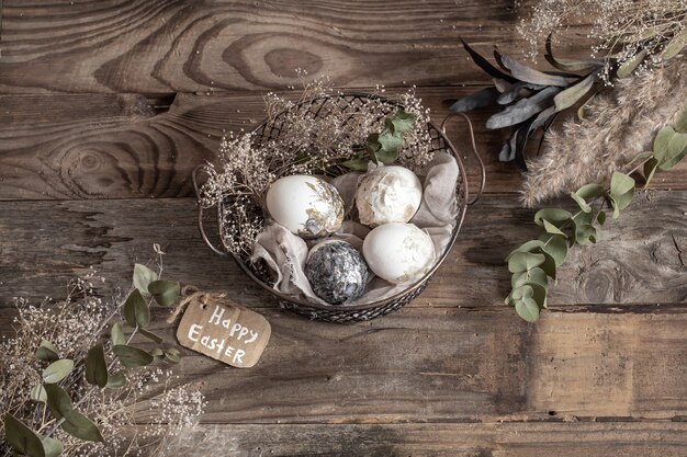 Huevos de Pascua en una canasta decorativa con flores secas sobre una mesa de madera. Concepto de Pascua feliz.