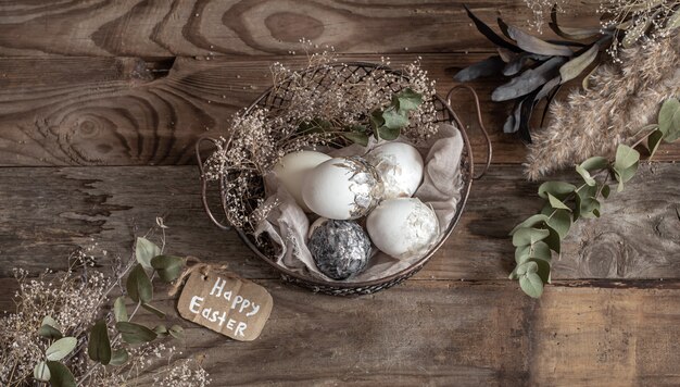 Huevos de Pascua en una canasta decorativa con flores secas sobre una mesa de madera. Concepto de Pascua feliz.